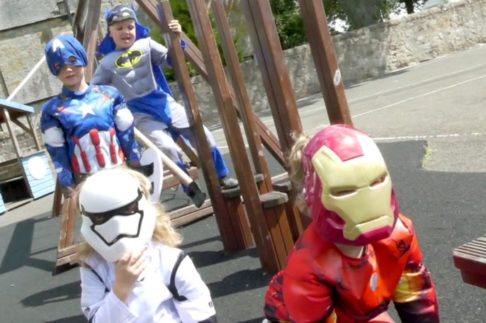Children dressed as superheroes in a playground.