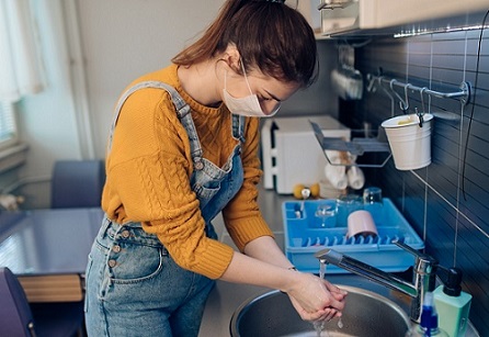 Housing support worker wearing a mask and washing her hands in a kitchen