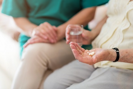 A person is supported with a glass of water and tablets in her own hand