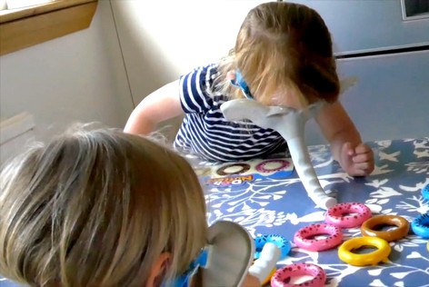 Children are playing a tabletop game where they pick up rings using elephant masks with trunks.